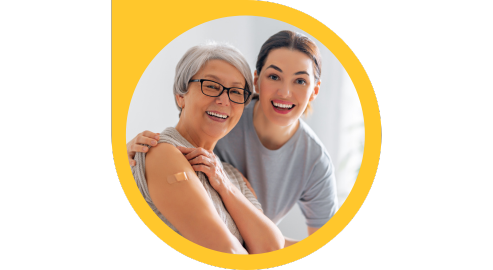 A smiling adult puts there arm over the shoulder of a senior, who holds up their sleeve to reveal a band aid over their injection site.