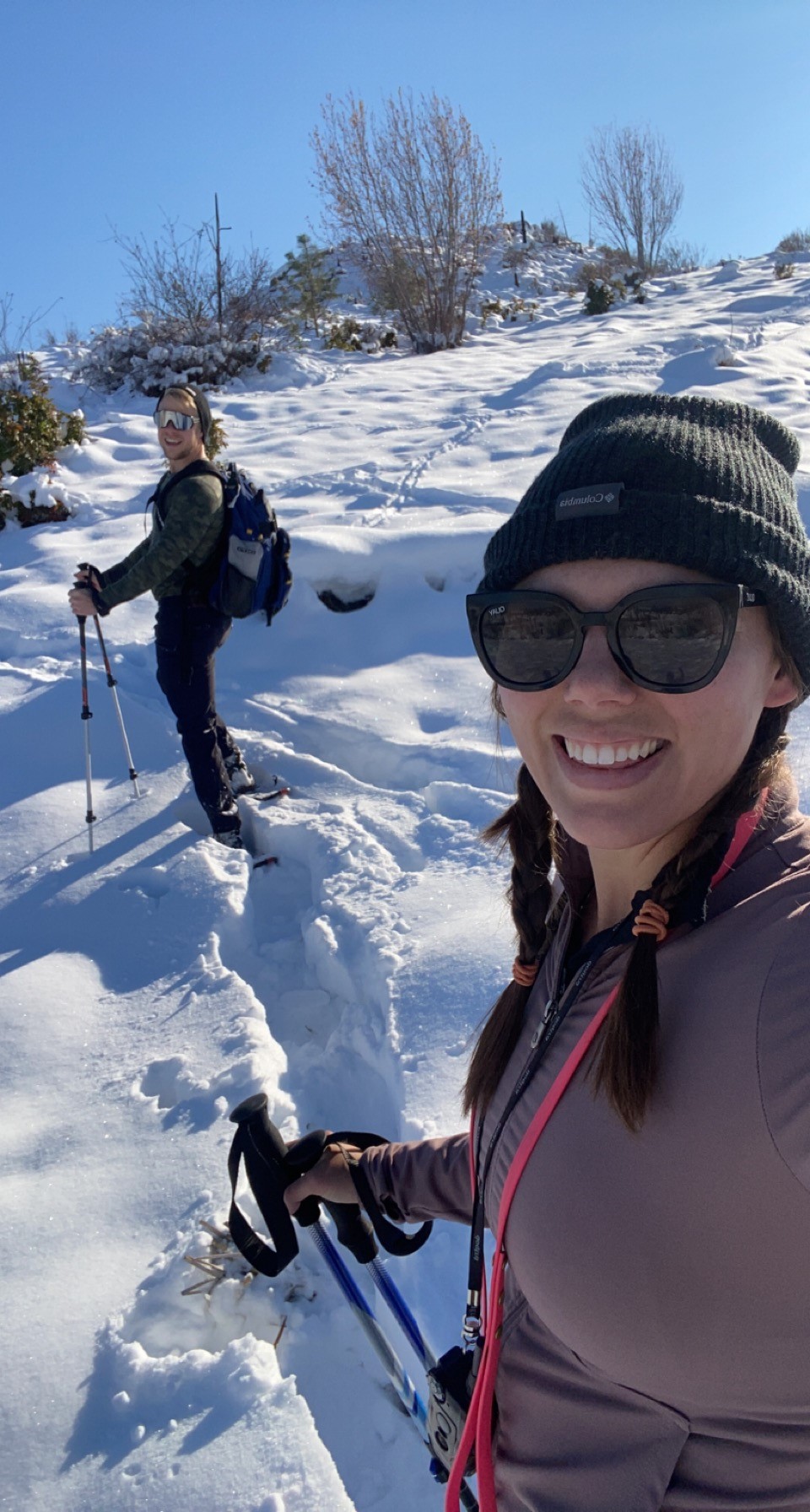 A person taking a selfie in the snow while snowshoeing, with another person in the background.