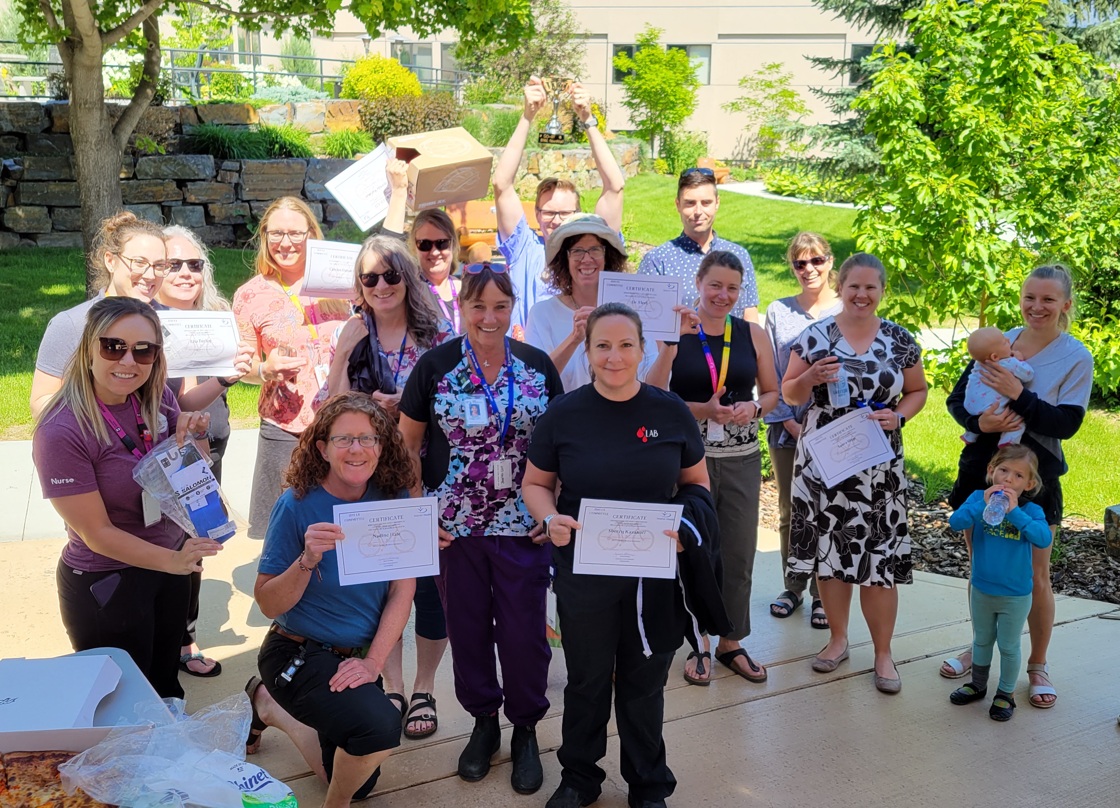 A large group of people stand holding certificates in their hands on a sunny day in a garden