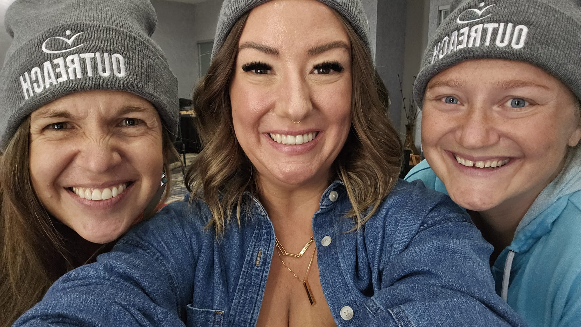 Three smiling people taking a selfie and all wearing a grey beanie that says OUTREACH.