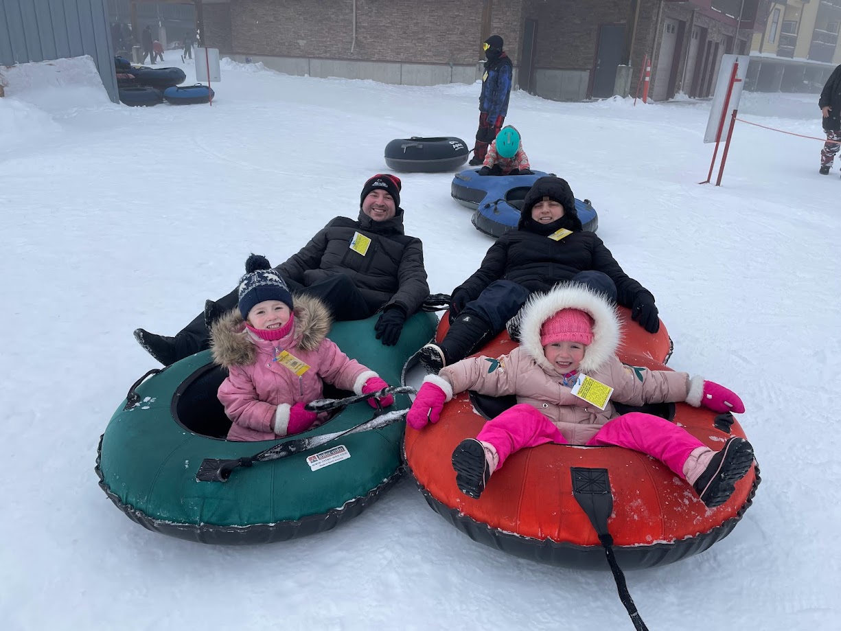 Four individuals enjoying a winter day on colourful snow tubes, with snowy surroundings.