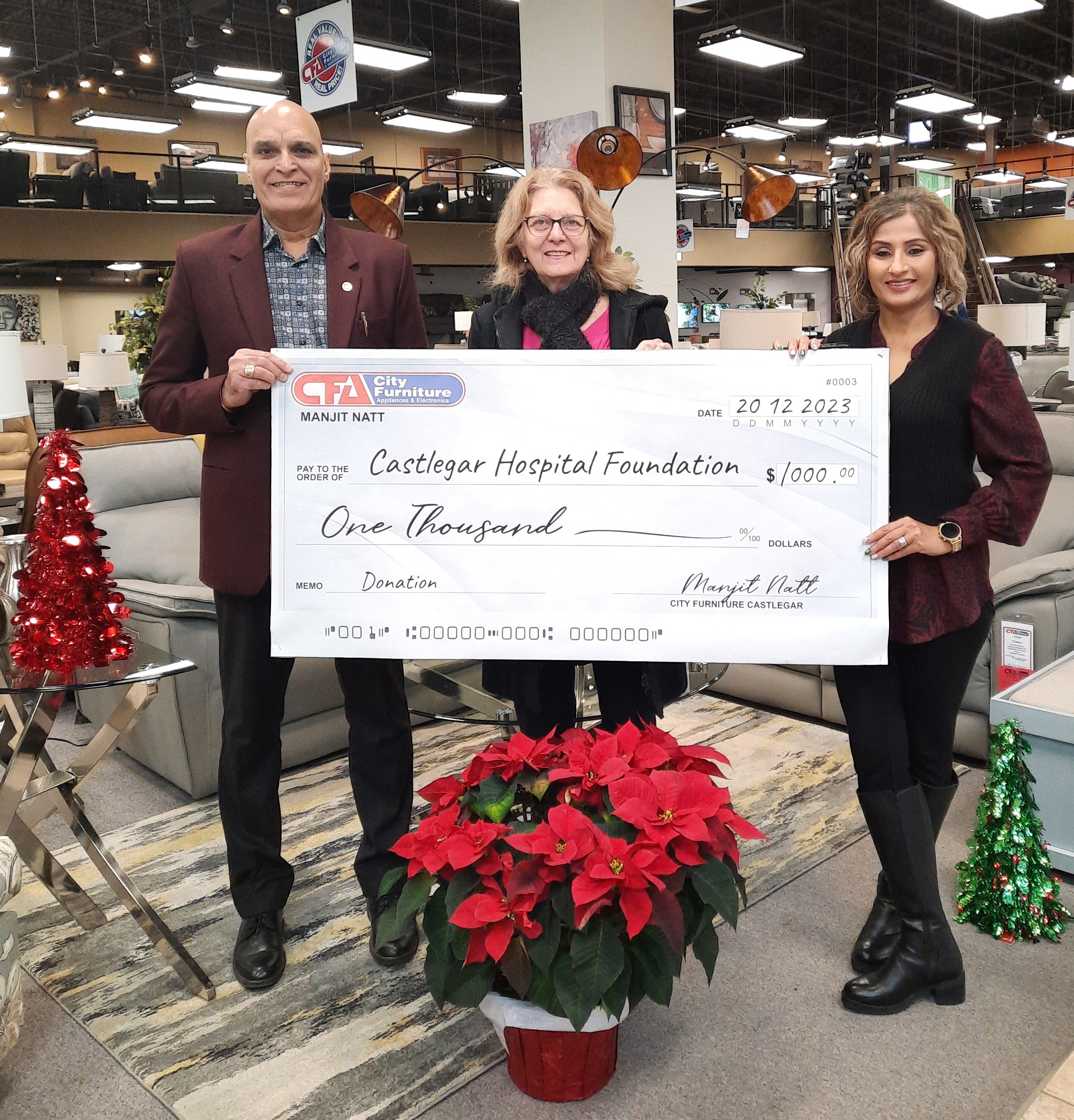 A group holds a large cheque showing a $1000 donation during the holidays.