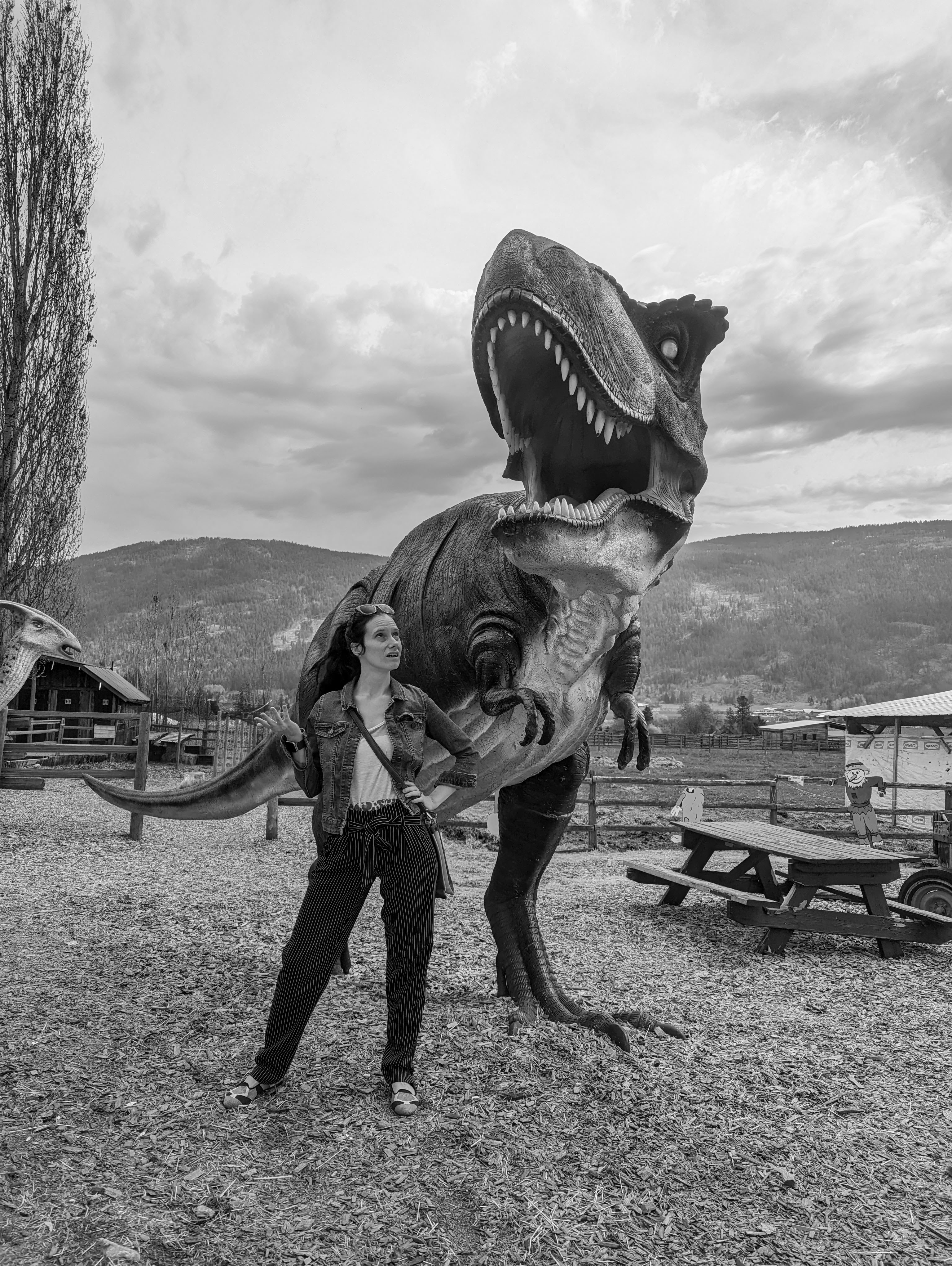 A black and white photo of a women standing next to a life size dinosaur statue.  