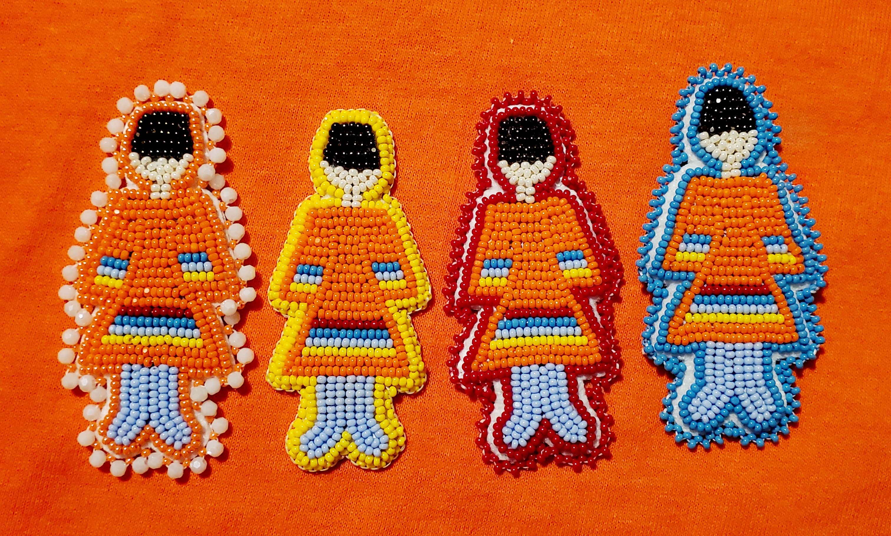 Four intricate beaded pins of basket hat women wearing orange beaded dresses with different shades of blue beads and yellow beads on their sleeves and on the bottom of their dresses. 