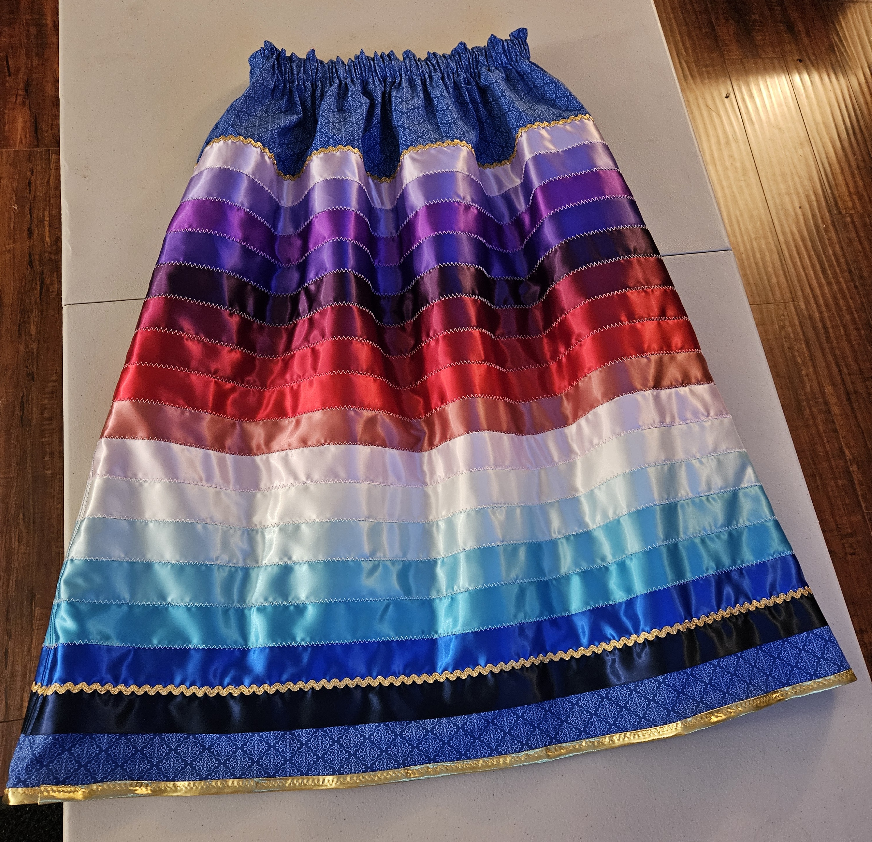 A photo of a blue ribbon skirt with different shades of purple, red, pink and blue ribbons lying on a table.