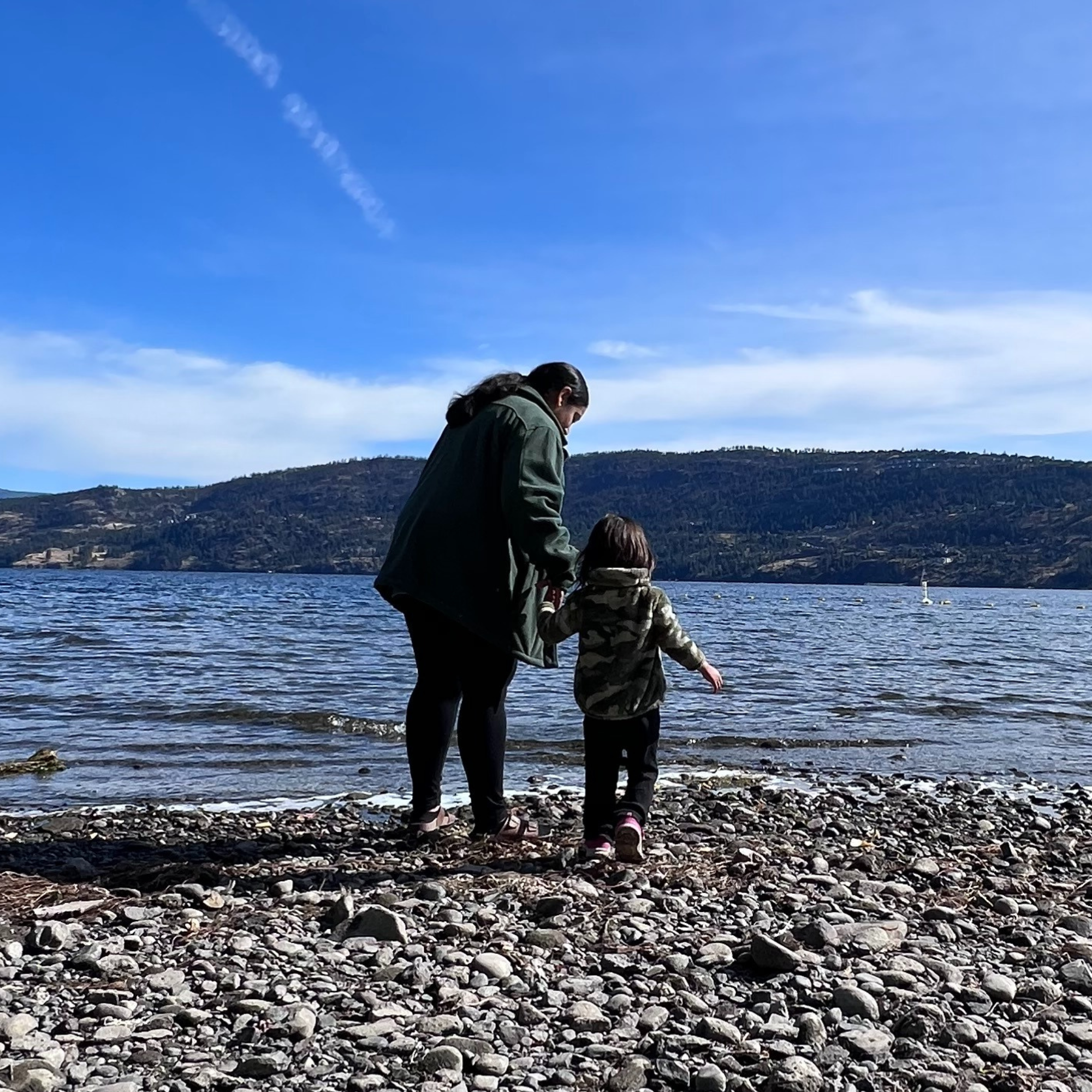 A woman and her toddler face away from our view while walking towards a lake at Bear Creek, B.C. in the autumn.