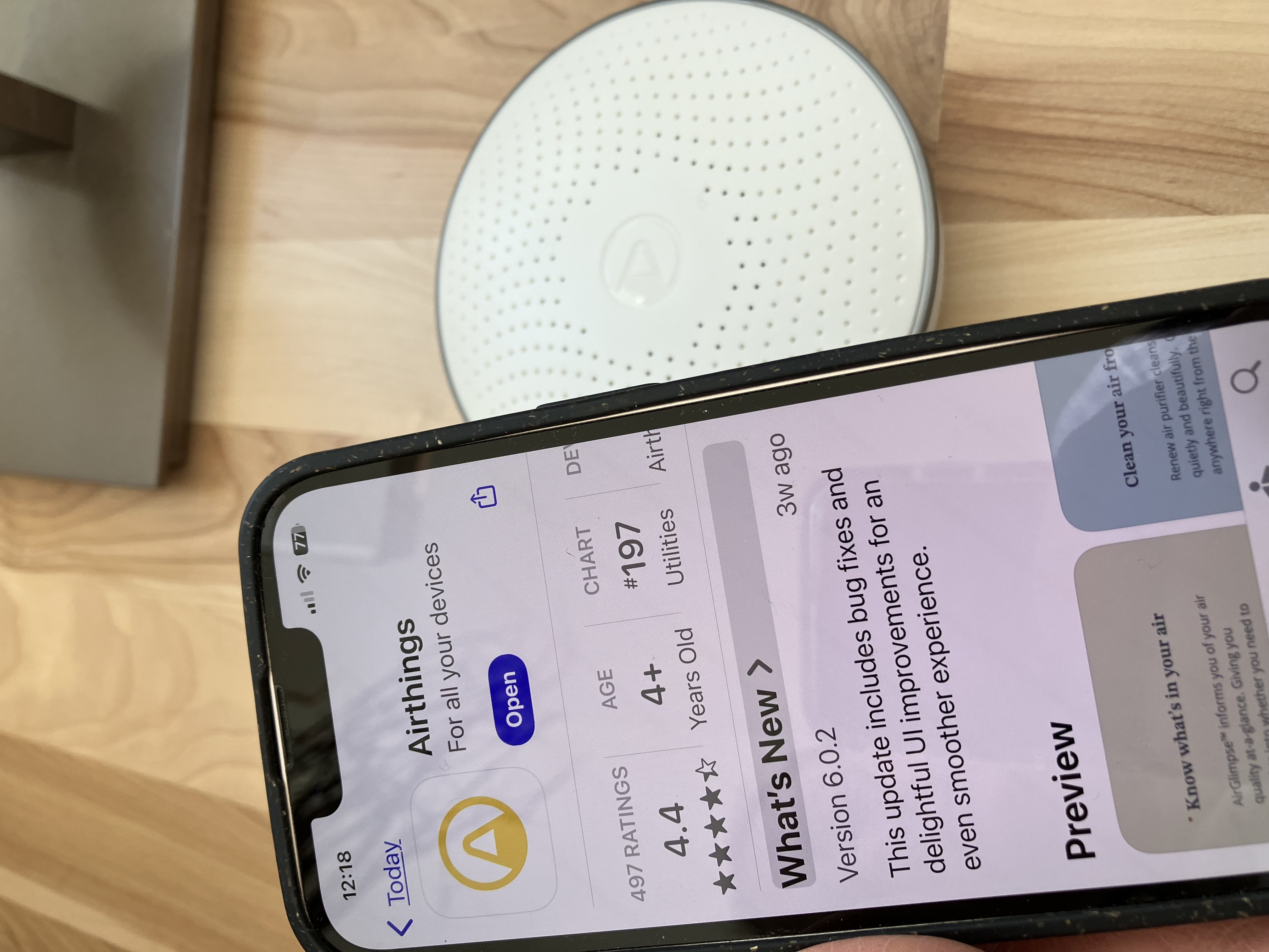A smartphone displaying the app page for 'AirThings' on its screen, placed next to an AirThings device on a wooden surface.