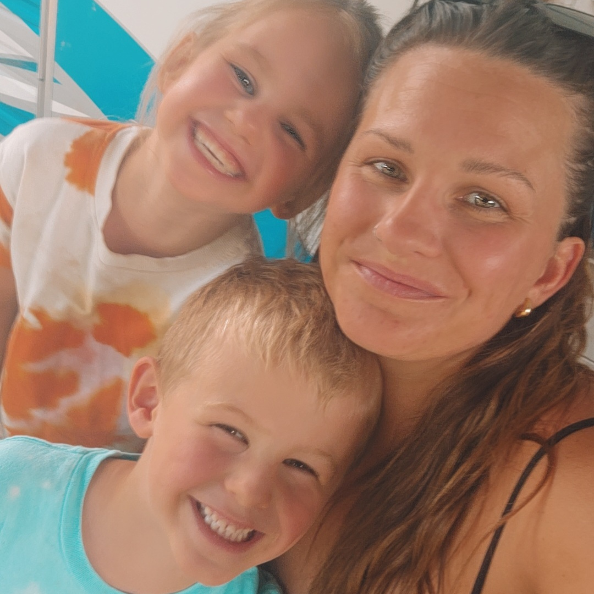 A woman wearing a tank top smiling with her happy son and daughter. 