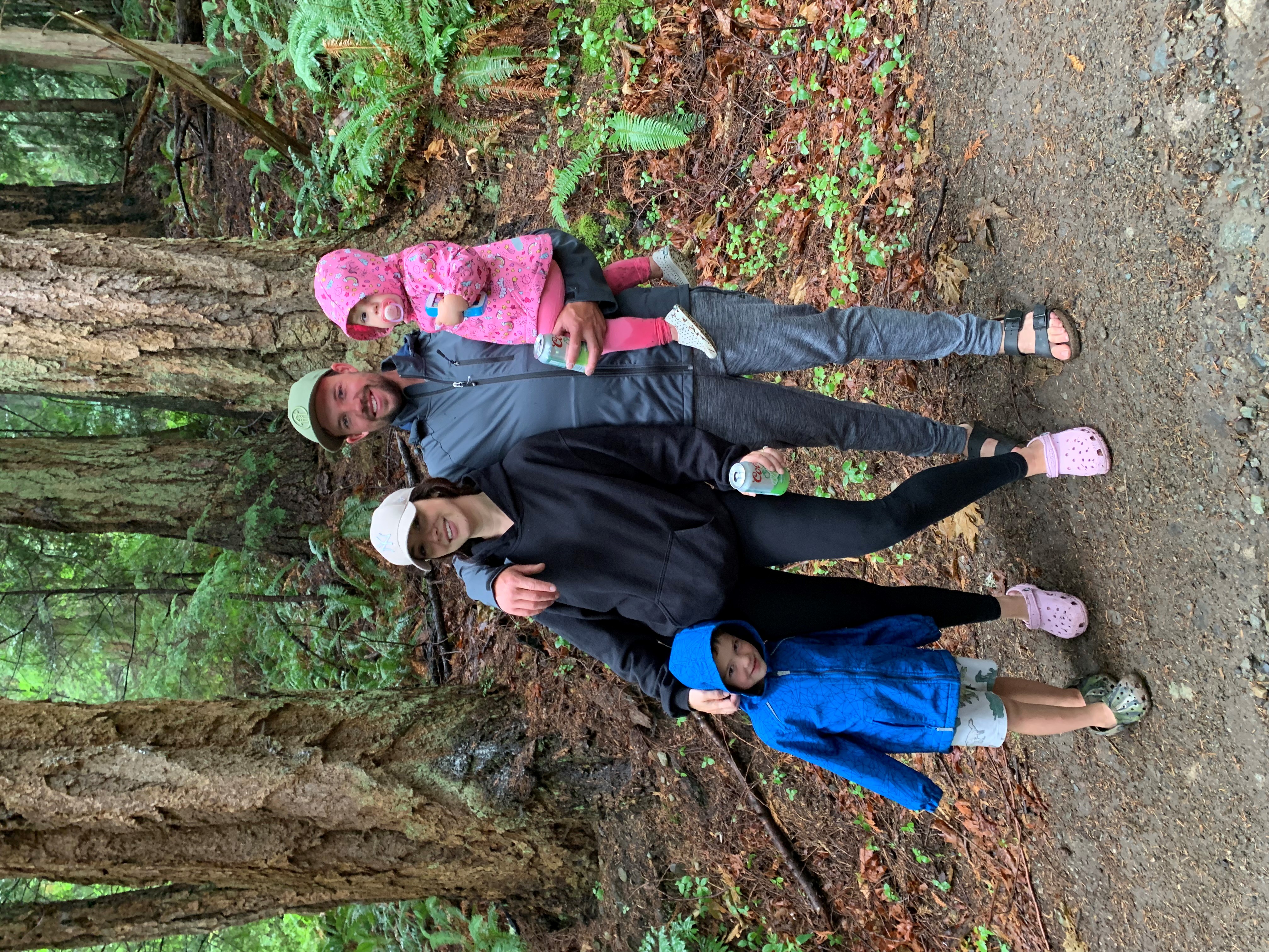 A woman and man in warm clothing and hats pose with two children in a forest