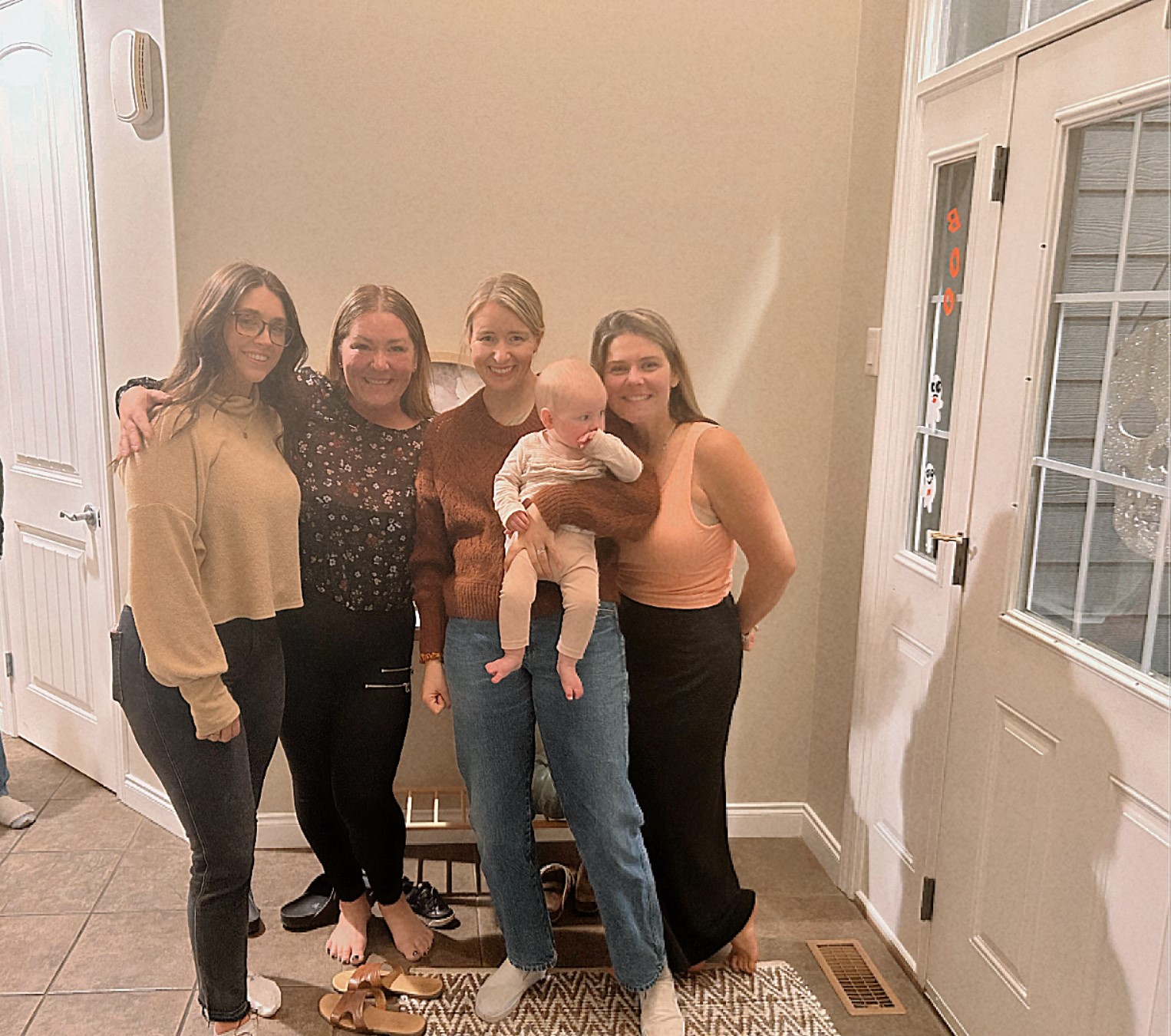 Four adults holding a baby standing together in a home entryway, smiling.