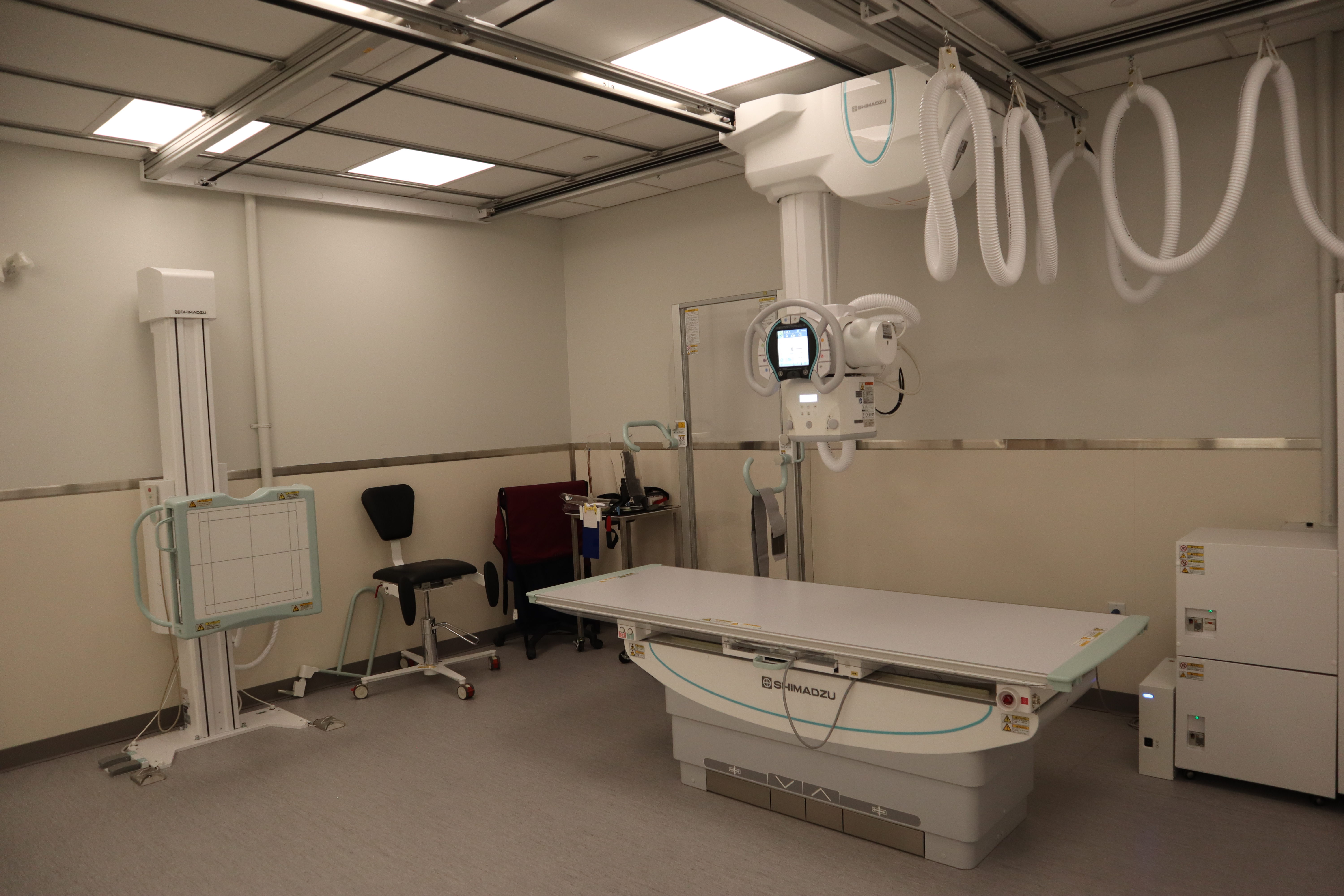 A medical room featuring an examination bed and large machinery hanging from the ceiling.