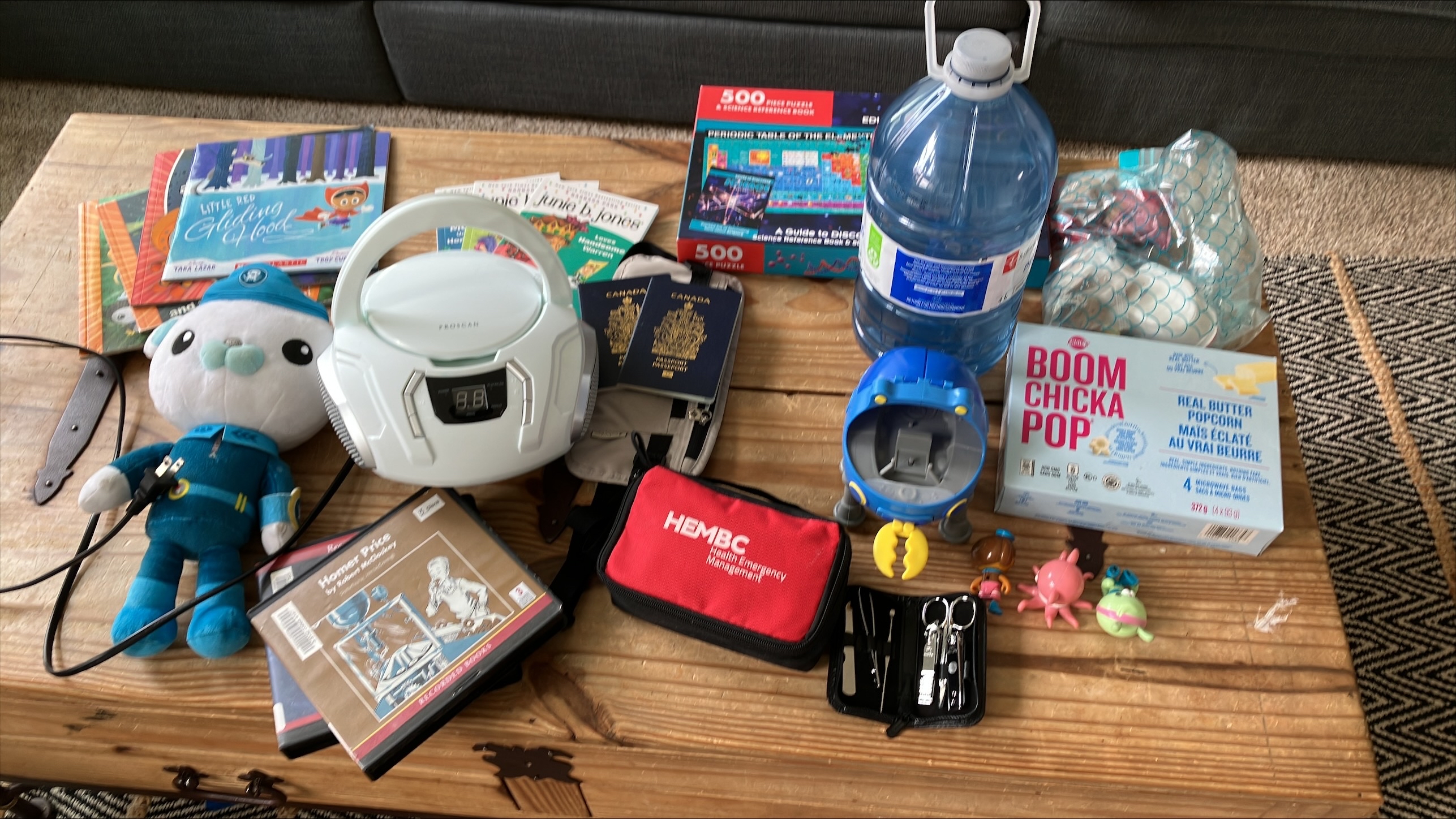 Soft toy, children’s books, small white radio, passports, bottle of water, and other items lying on a table