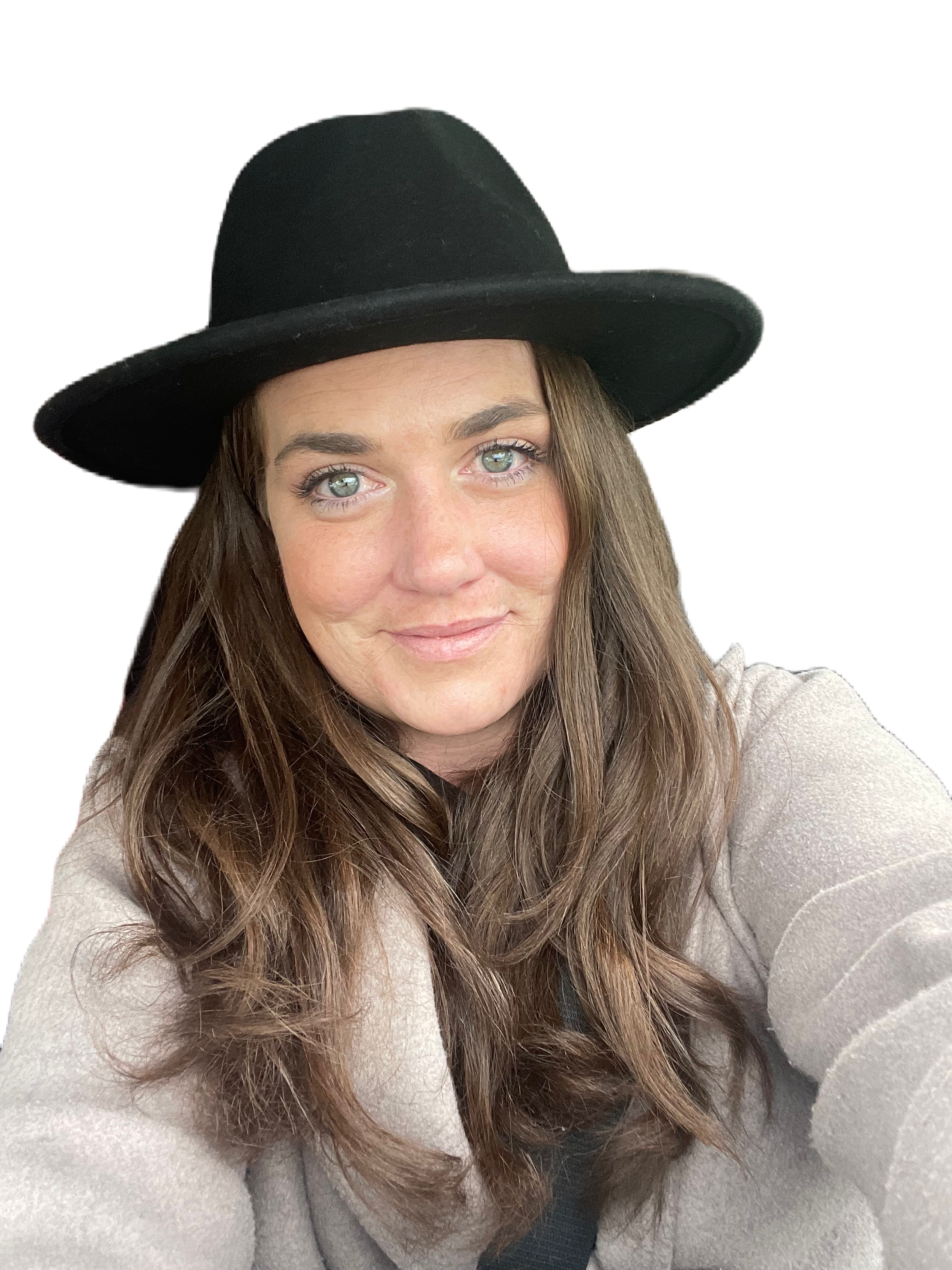 A smiling person with long brown hair and green eyes wearing a light grey sweater and black rimmed hat