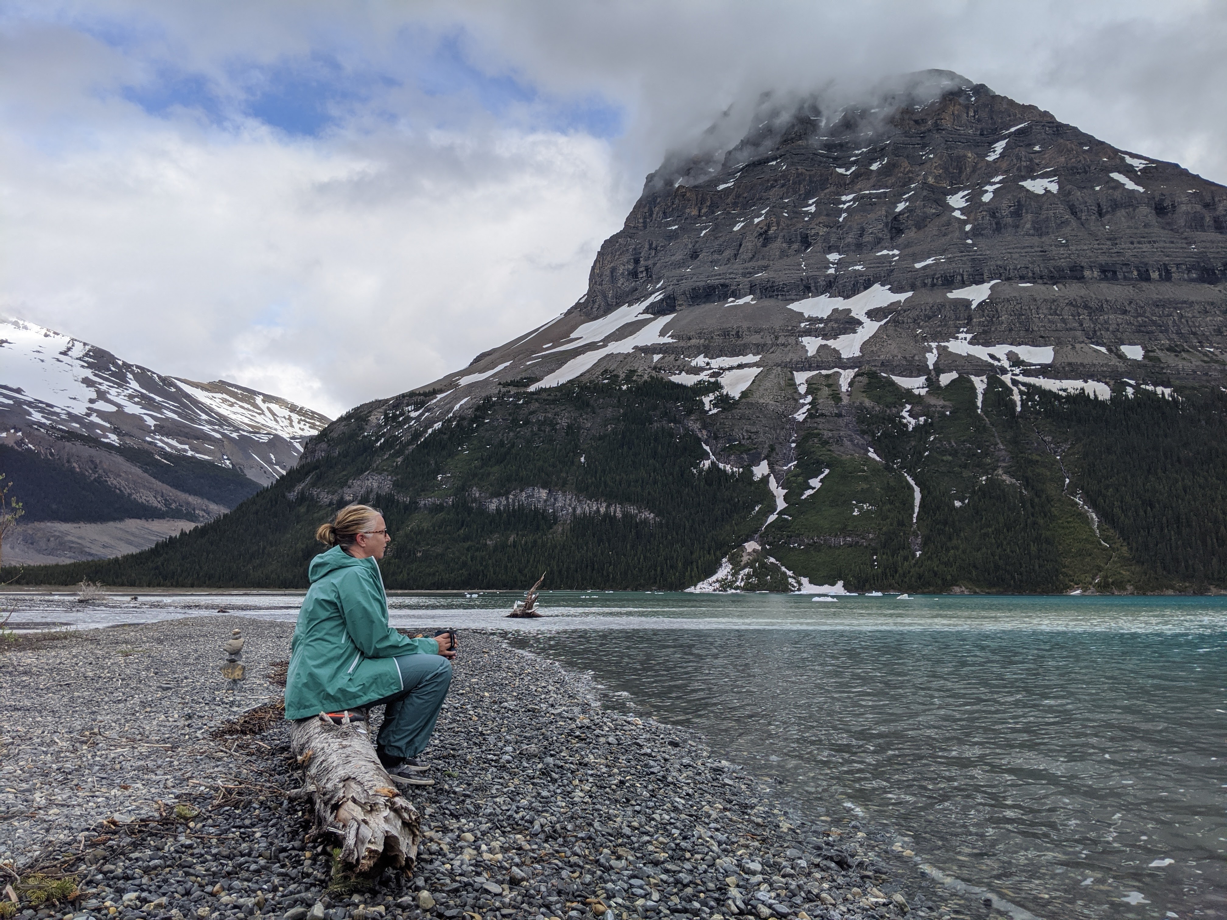 A woman sitting on a rock overlooking water and mountains