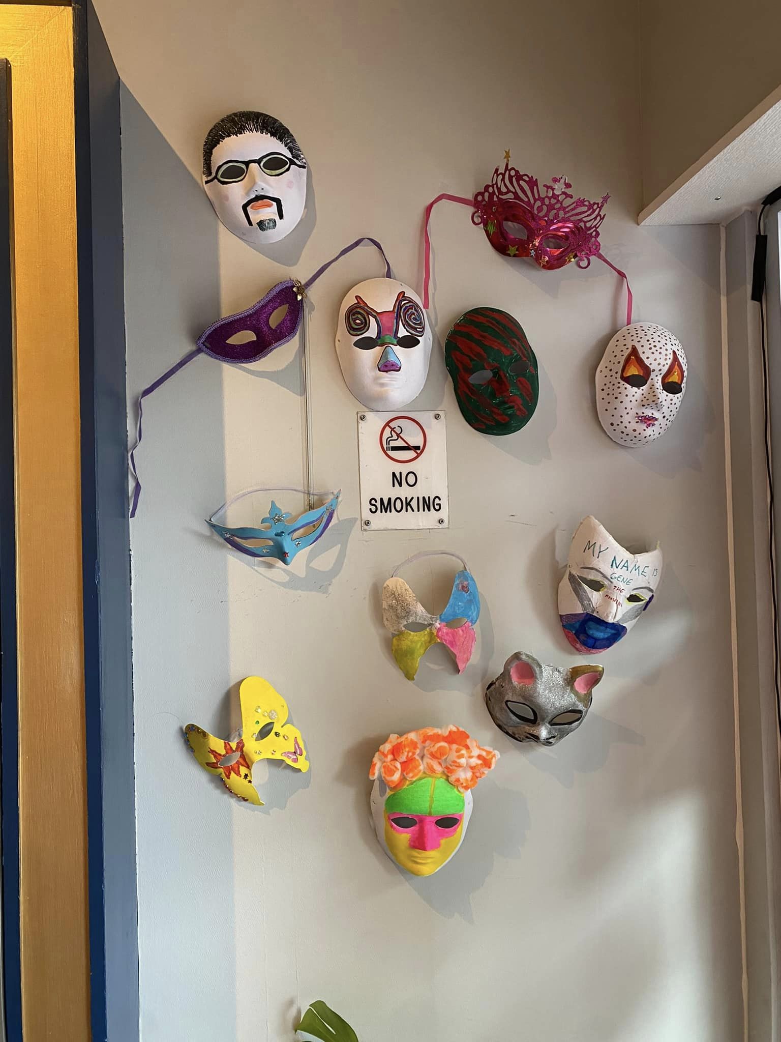Various colourful masks of faces, cats and butterflies on a beige wall