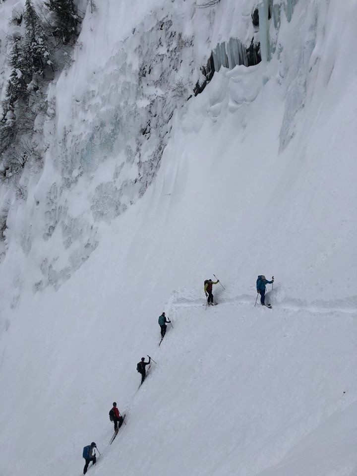 A group of climbers ascending a steep, snow-covered slope with icy patches, using climbing axes and ropes for safety.