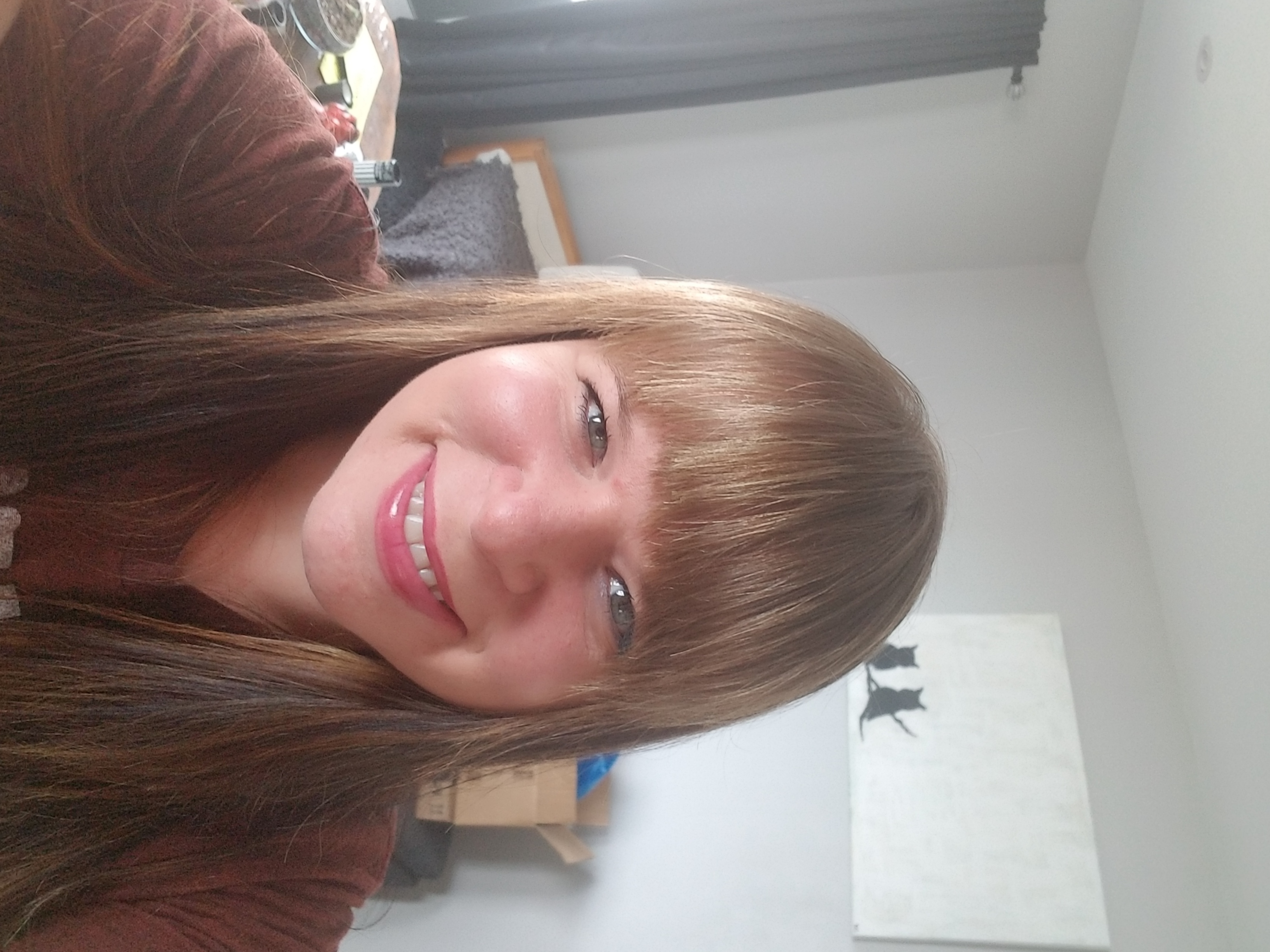 A selfie of a smiling woman with long, light brown hair who is wearing a maroon shirt.