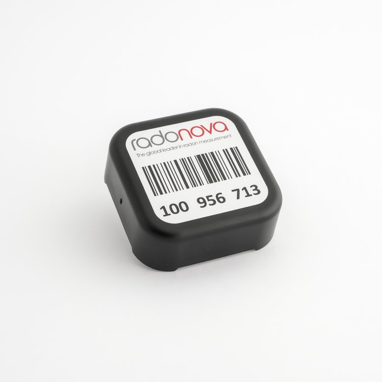 A Radonova black radon detector with a barcode and identification number displayed on top, set against a plain white background.