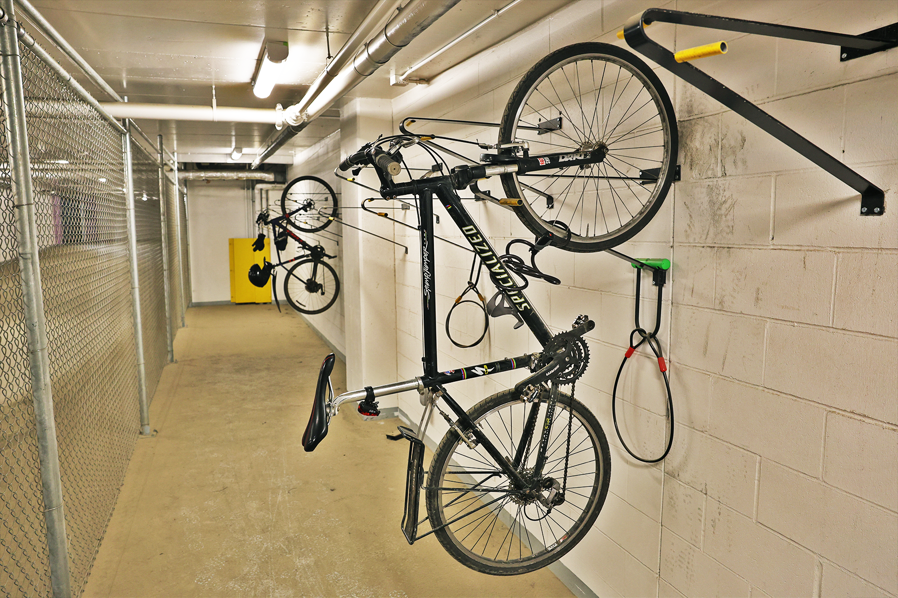 Two black hybrid bikes suspended on racks against a white brick wall