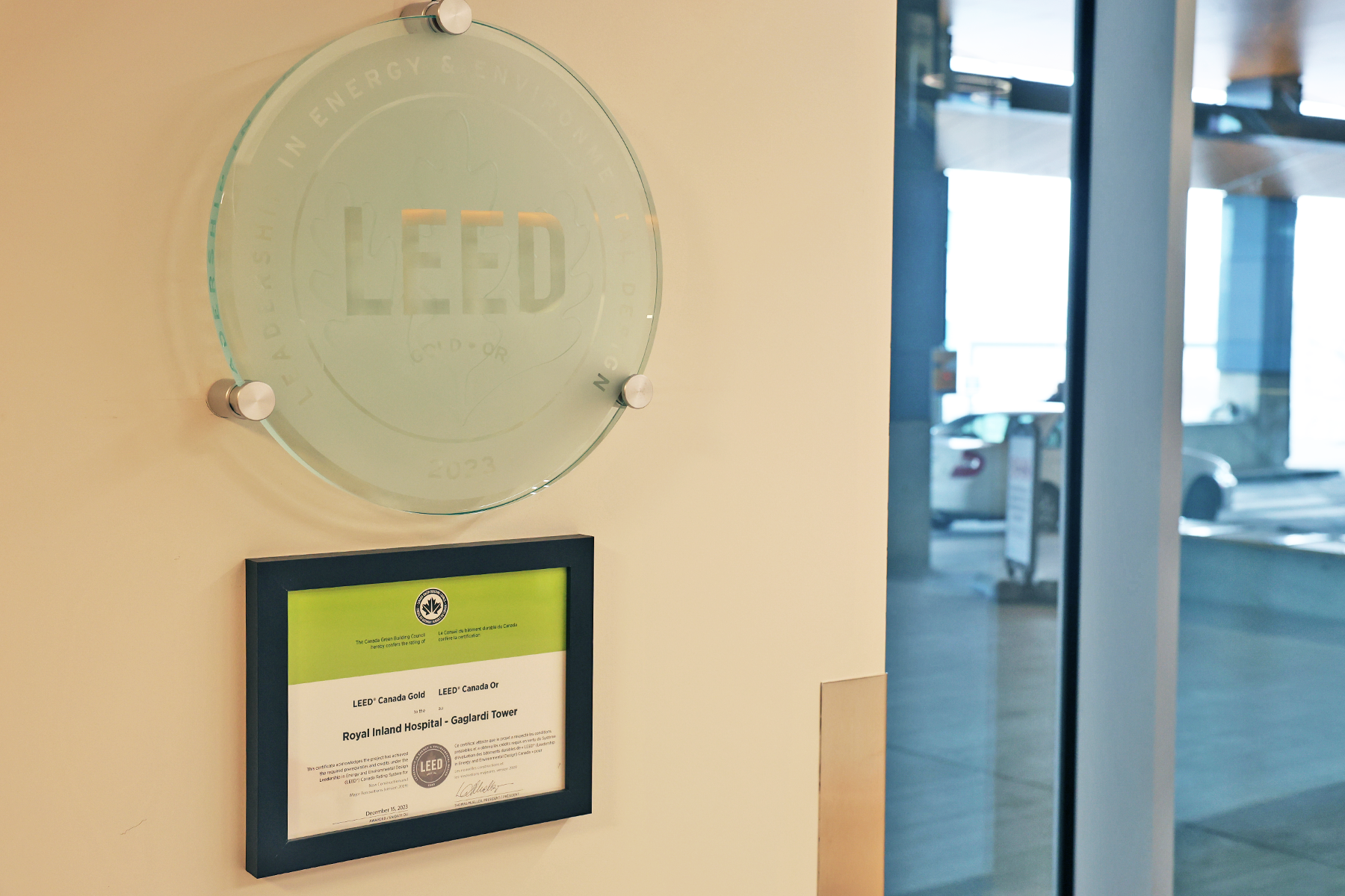 A round glass plaque with the word LEED above a green and white framed certificate hangs on a wall.