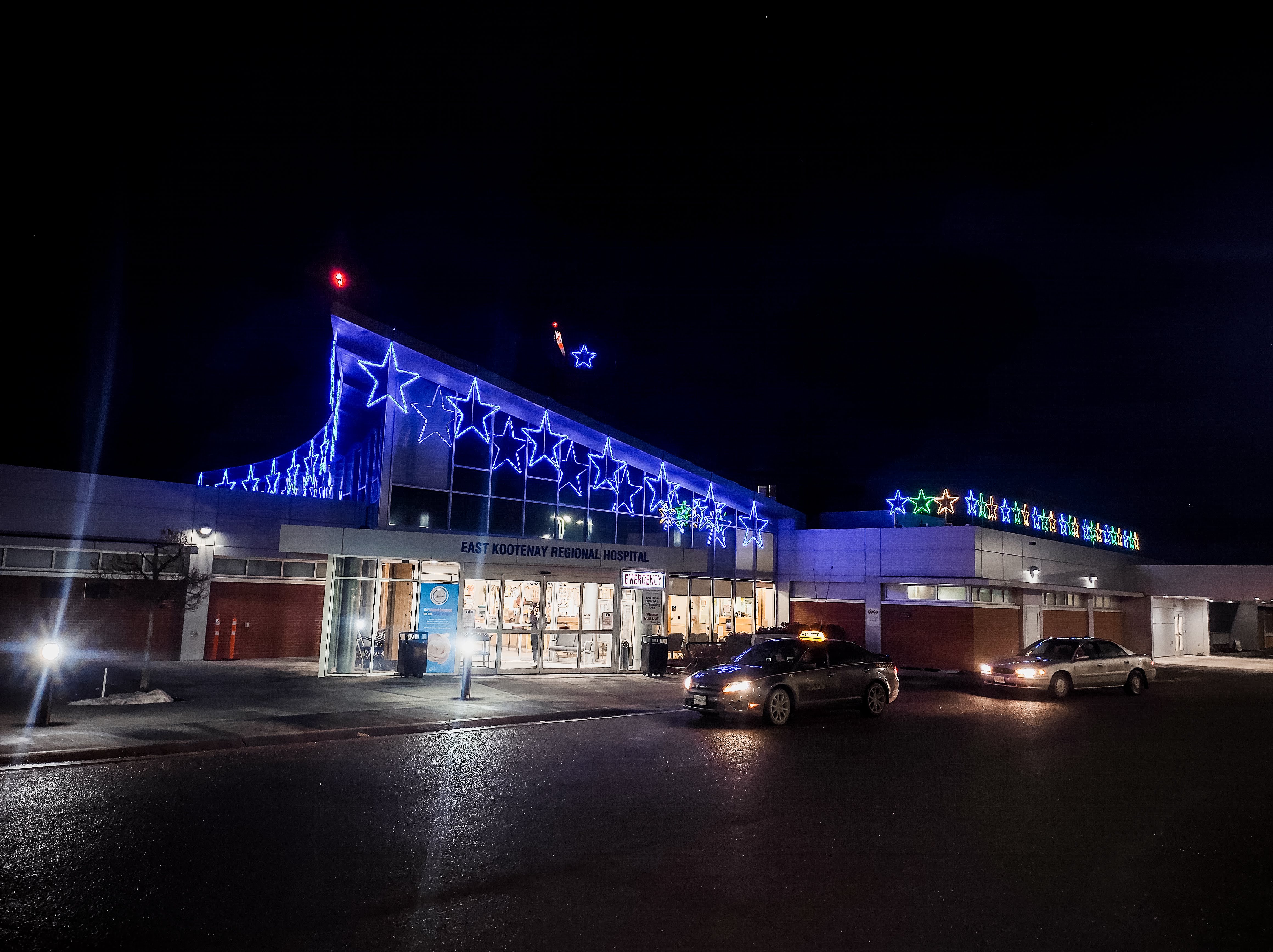 A photo of the East Kootenay Regional Hospital building taken at night lit up with blue and yellow stars along the roofline.