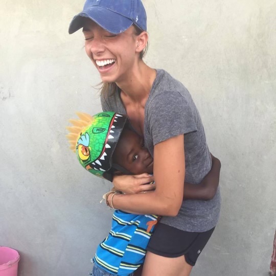 Woman with a big smile on her face laughing as she is hugging a small boy in a dinosaur helmet