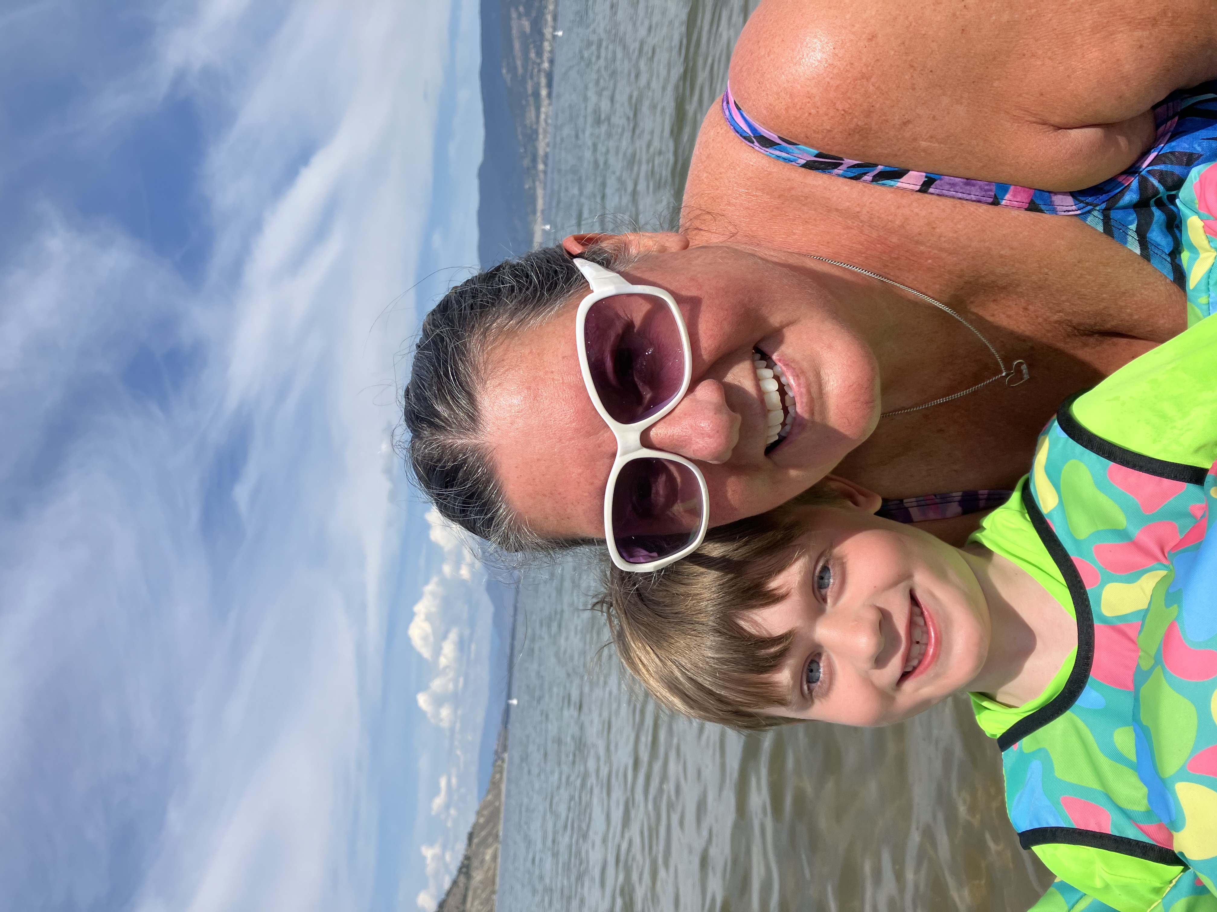 A woman with a child in brightly coloured swim gear in a lake. 