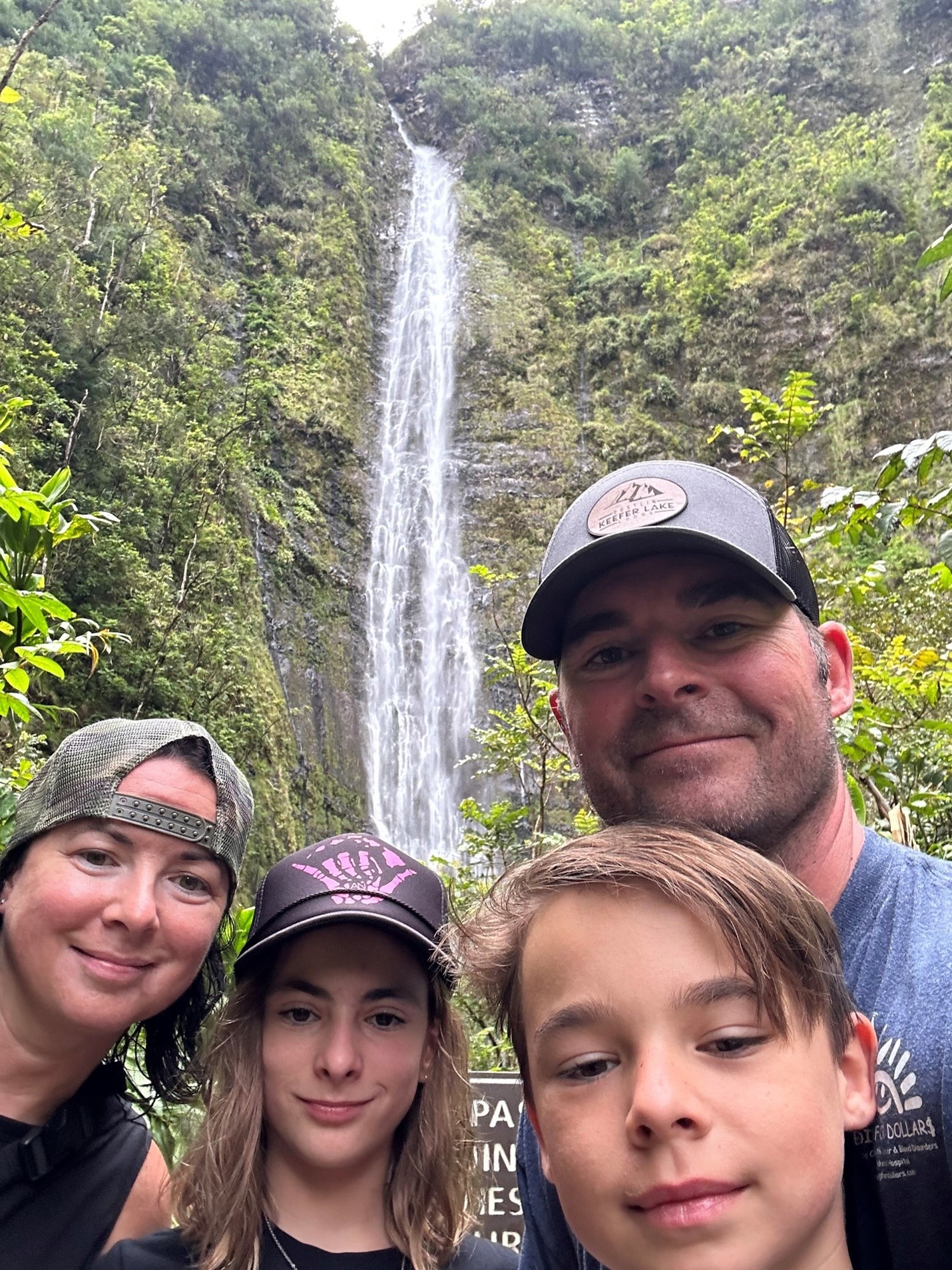 Woman, man, girl, and boy stand in front of waterfall in lush forest