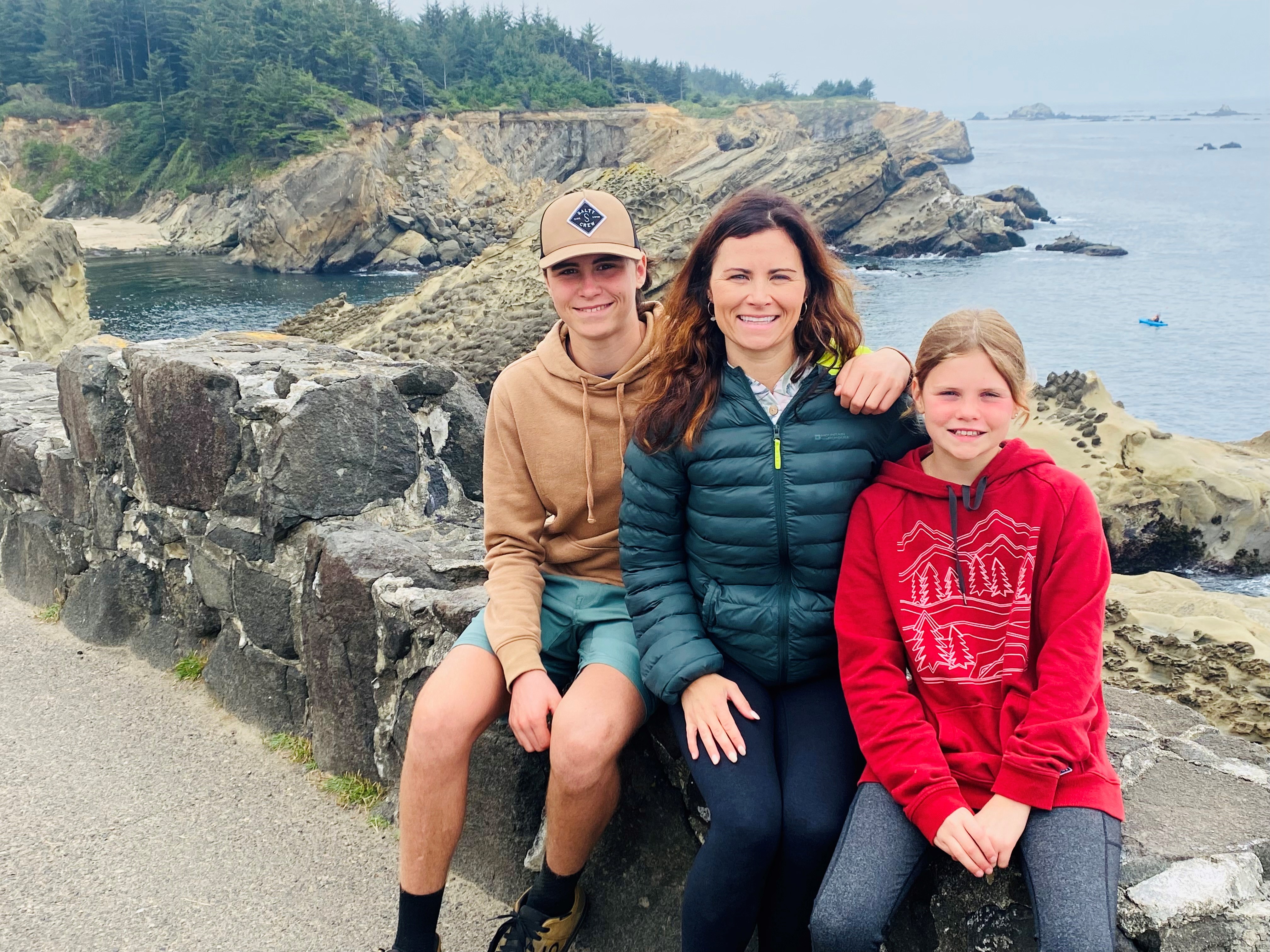 Three people sitting on a rock looking over the water.