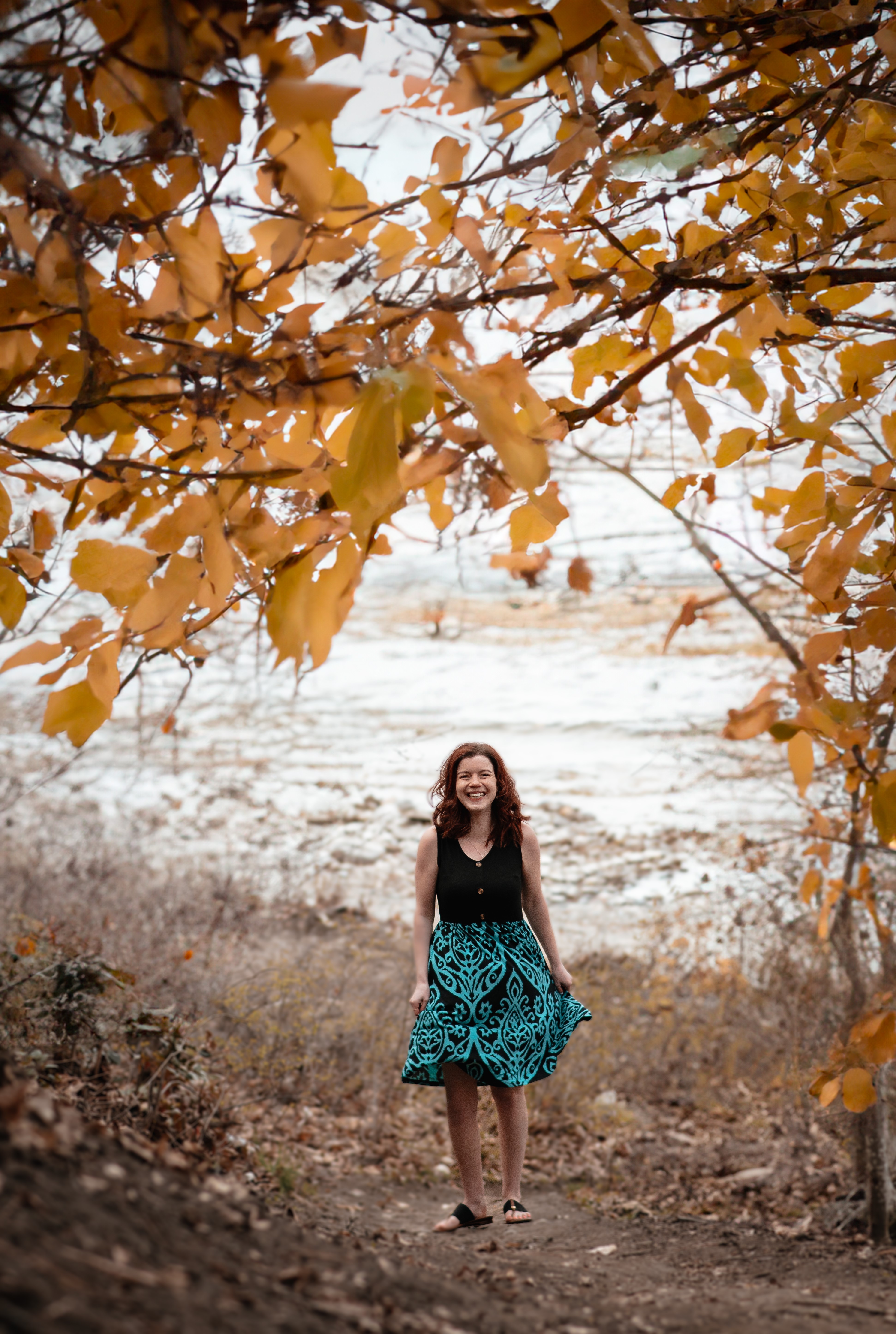 Woman in black and turquoise dress standing under a tree with lake in background