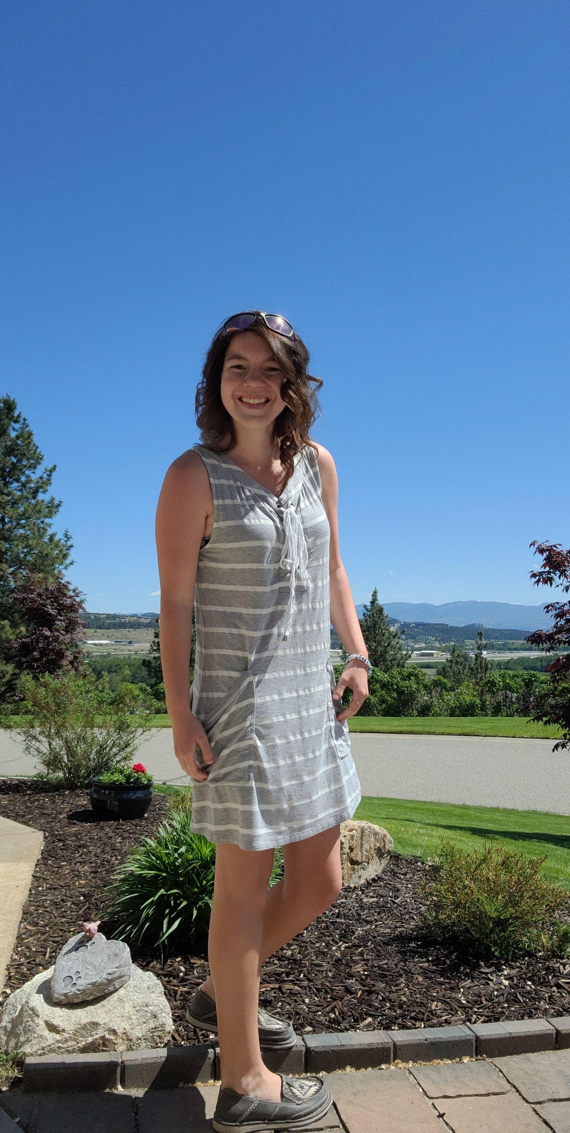 Woman in grey striped summer dress standing on paved path in the sunshine