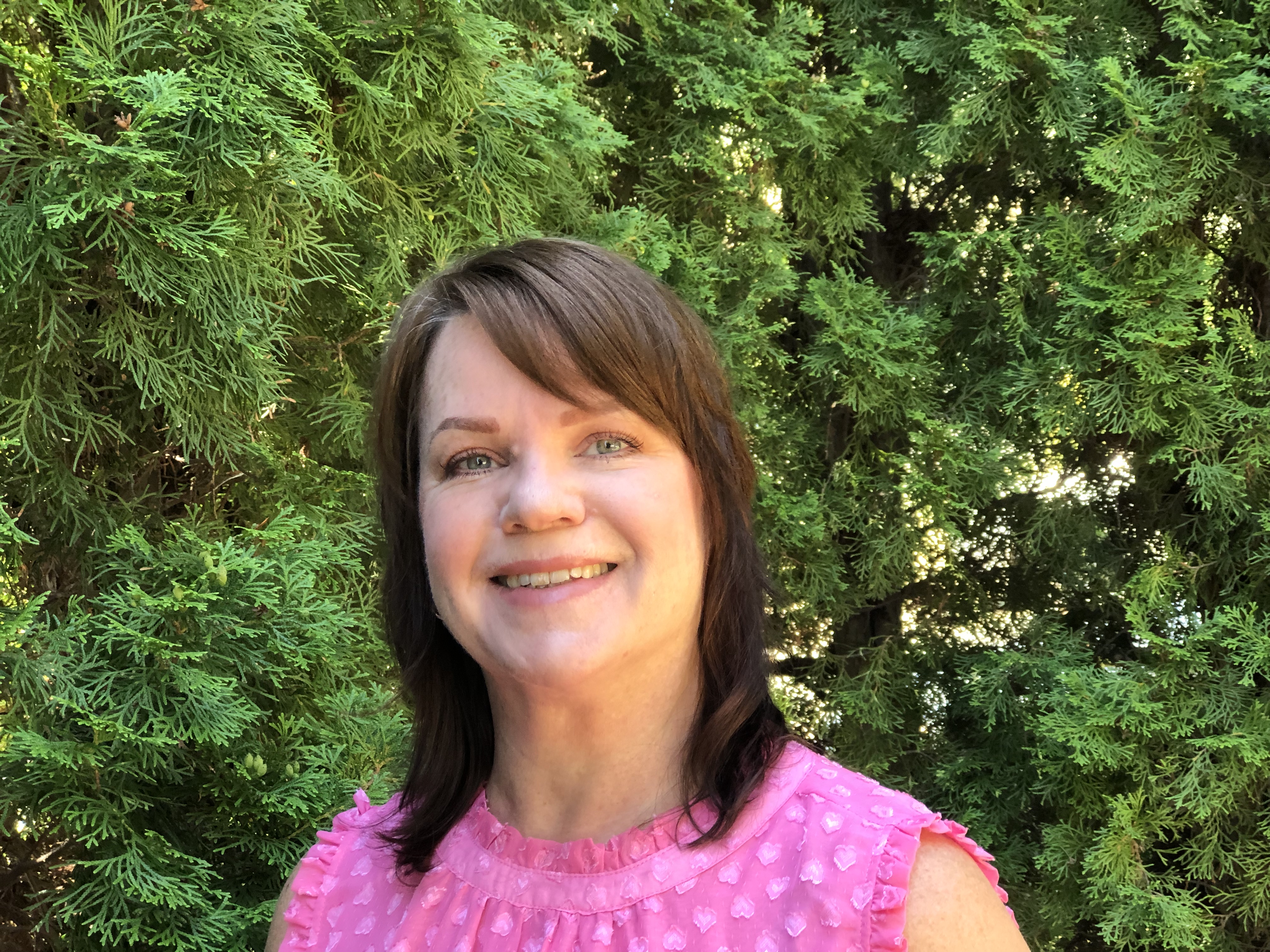 A profile shot of a smiling woman with brown hair and wearing a pink summery shirt. 