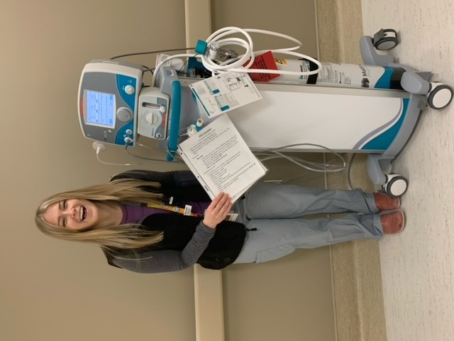 Smiling young woman stands next to a respiratory machine in hospital.