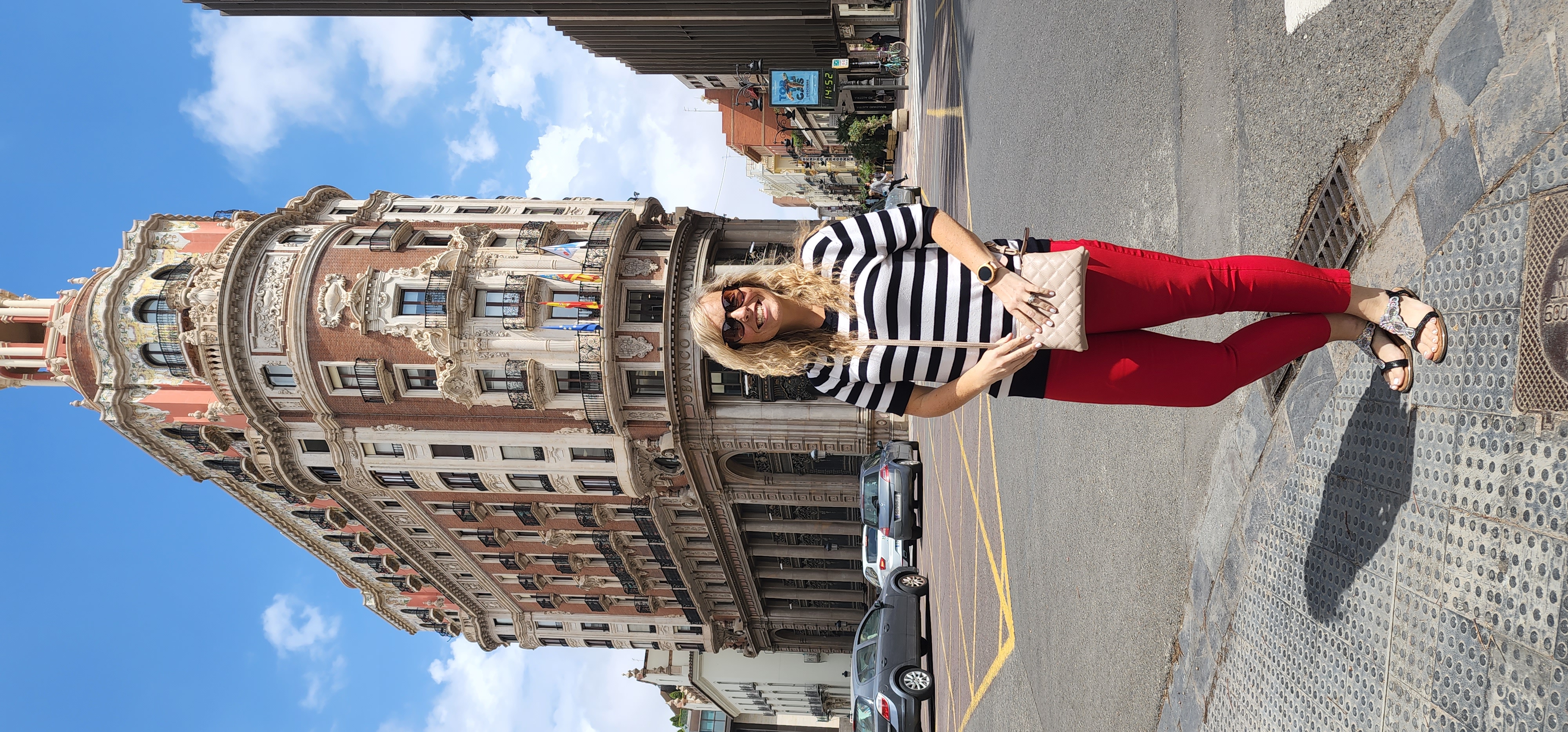 A woman poses for a picture on the streets with an ancient building in the background.