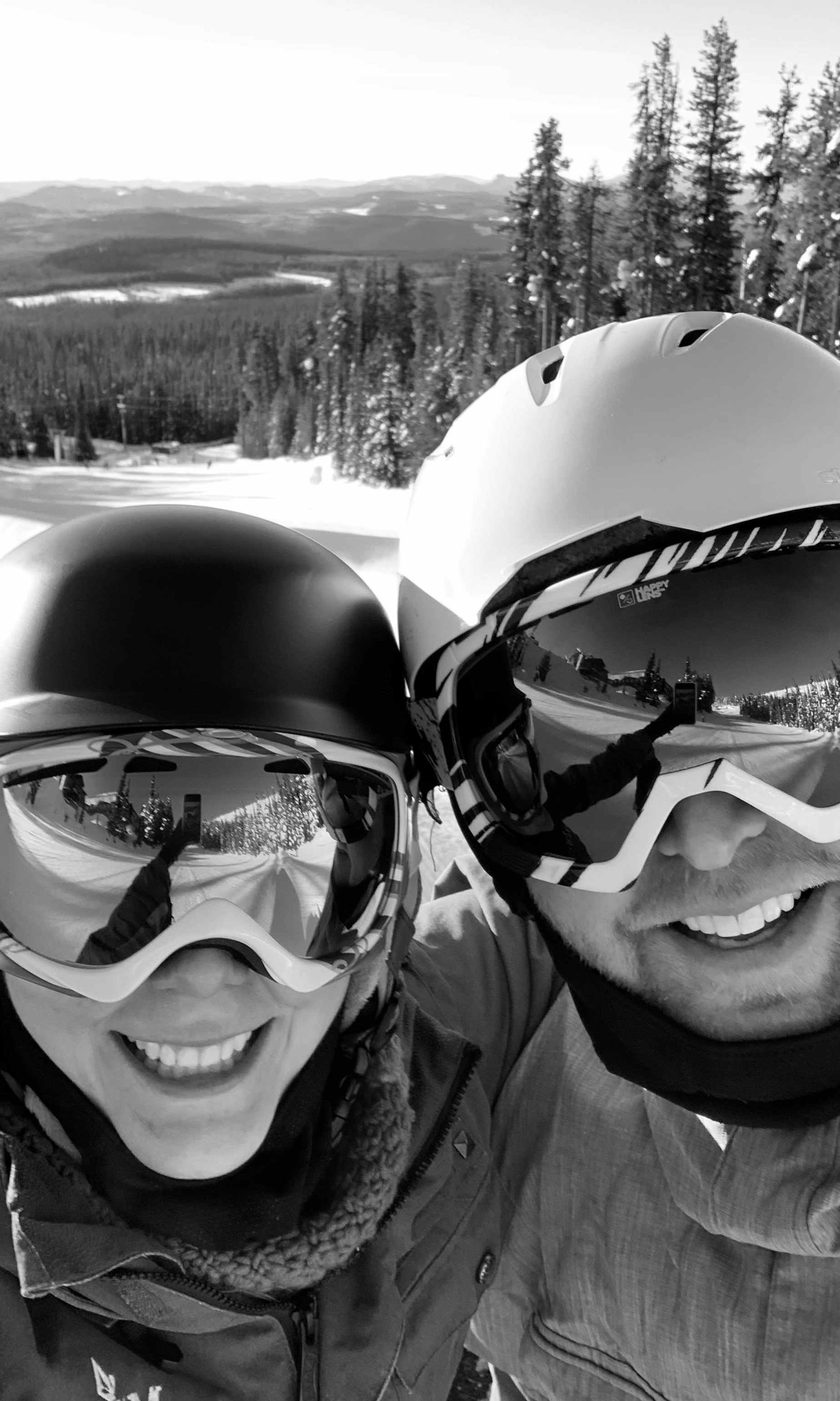 A black & white close-up of two people wearing ski gear, on a ski hill.