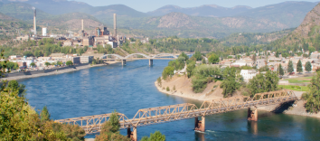 A landscape shot featuring two separated bridges over a body of water with groups of buildings on both sides and mountains in the background.