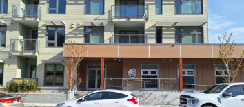 A three story beige building with an orange portico and three cars parked in front