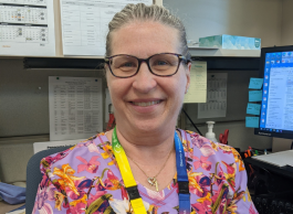 Smiling woman wearing scrubs, sitting at a desk.