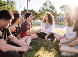 Teens have a conversation while sitting on grass.