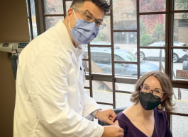 A woman gets a band aid placed on her upper arm by a health-care professional after getting a vaccine.