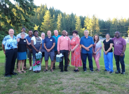 A group of people standing in the grass at a park, two of them holding presents.