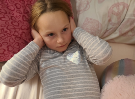 A child lying in bed with their hands over their ears.