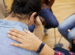 A hand rests on the shoulder of a person wearing a blue shirt and holding their head in their hand.