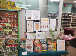 A display at the Westbank library that includes a shelf with dozens of seed packets, a table of books on gardening and seeds, and flyers and pamphlets.