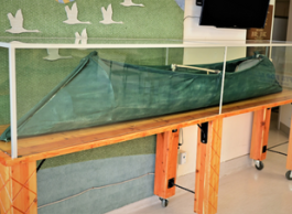 A green canoe under glass on a wood stand.