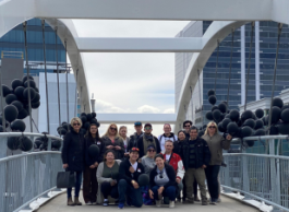 A group of people hold large bunches of black balloons while posing on a bridge.