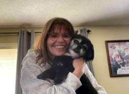 A woman smiles while holding her small dog.