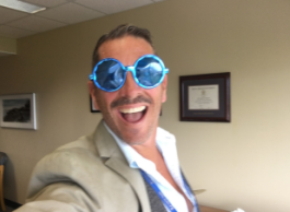 A man with short brown hair wearing a novelty sized pair of blue sparkly sunglasses