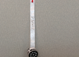 A black cylinder radon detector pinned to a board by a strip of white tape