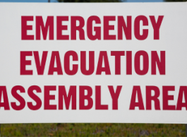 A white sign with red lettering that reads emergency evacuation assembly area